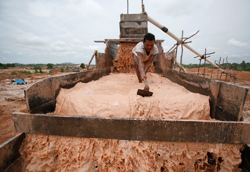 An illegal miner sorts tin ore from sand at a mining site, Indonesia