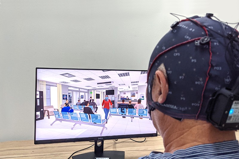 A man wearing an EEG watches a screen that shows a virtual waiting room