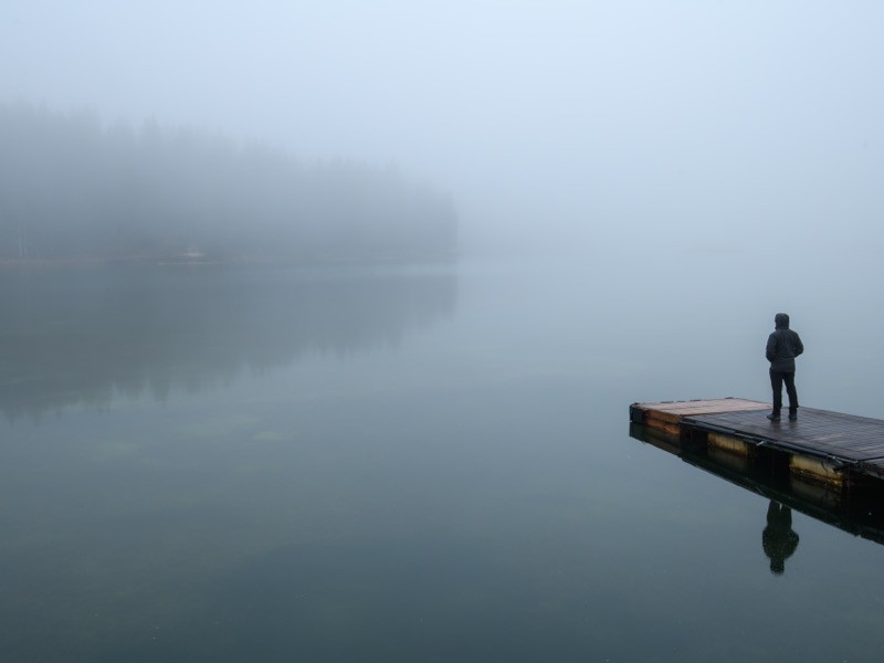 Side view of man standing on the bridge on a foggy winter day.