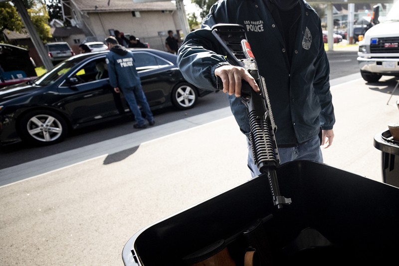 A Los Angeles police officer throws assault rifle into a garbage container on the street during an anonymous gun buyback event
