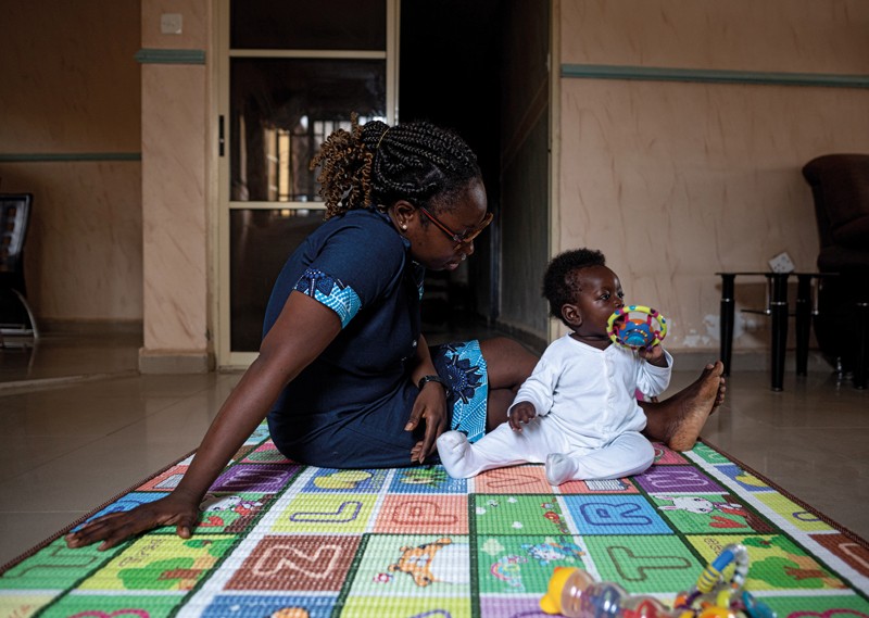 Sean plays with a toy on a bright play-mat as his mother looks at him in their living room in Nigeria