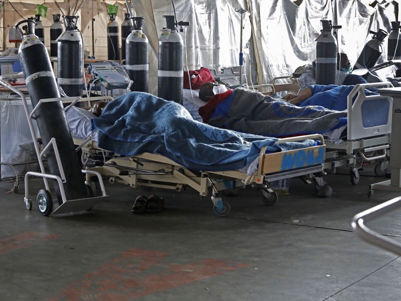 People lying in hospital beds, with oxygen cylinders.