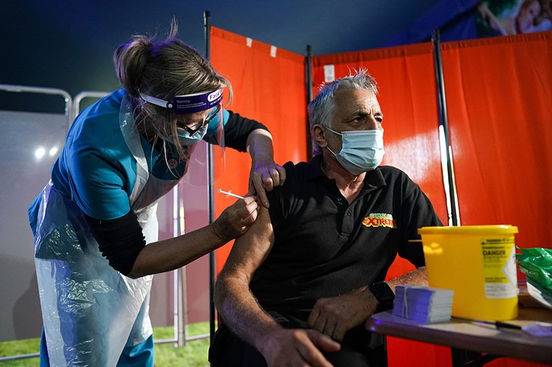 A doctor vaccinates a man in an outdoor clinic, at night.