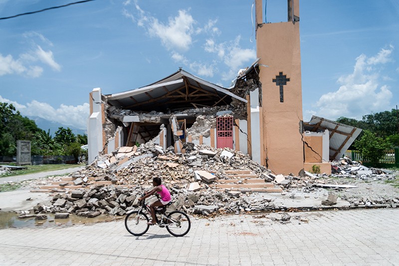 A child rides a bike on the road in front of a church that has been demolished by an earthquake in Chardonnieres, Haiti.