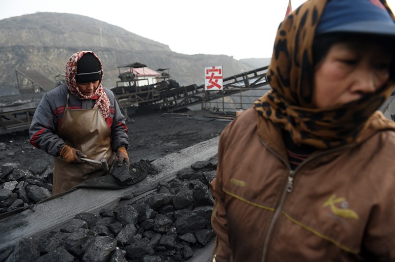 Workers sort coal on a conveyer belt, near a coal mine in China
