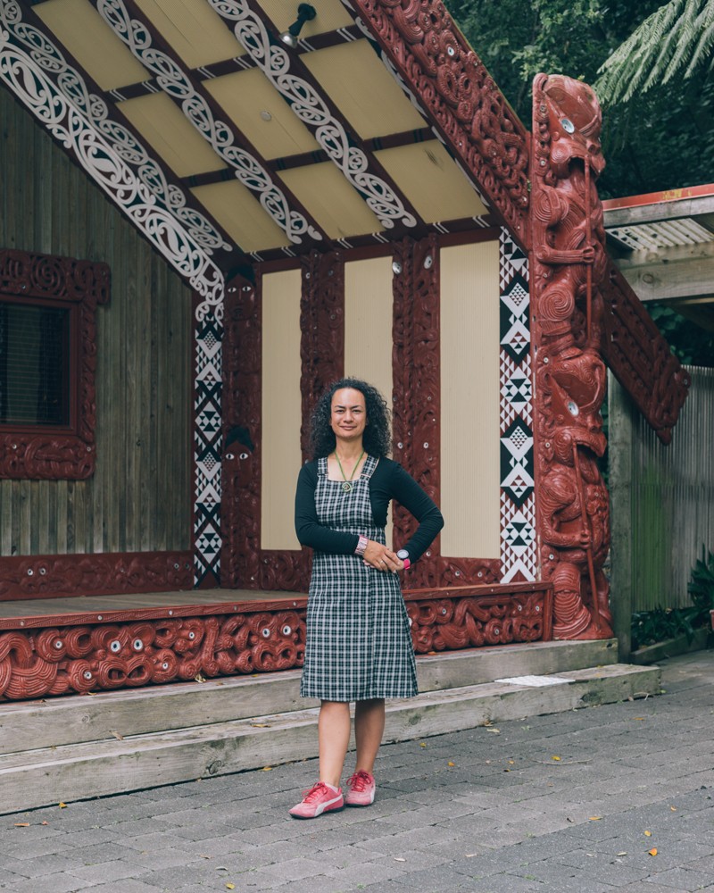 Ocean Mercier standing outside the wharenui of the University of Wellington, decorated with wood carvings and geometric panels
