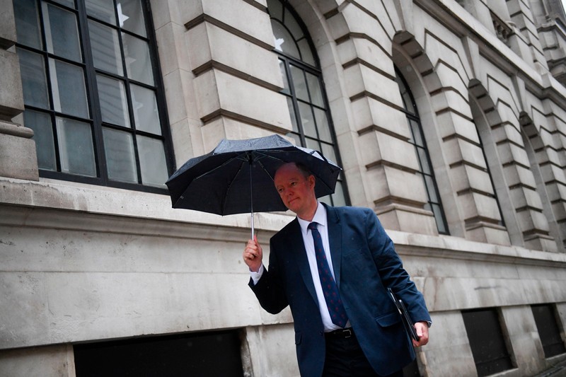 Chris Whitty walks through Westminster in London holding an umbrella