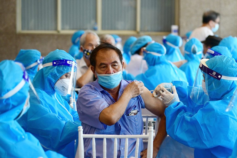 A man surrounded my medical workers in blue coveralls, face masks and visors, receives a covid-19 vaccine in Vietnam