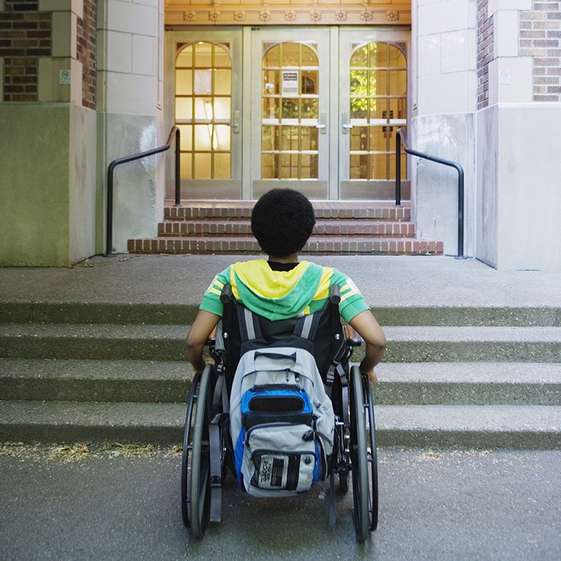 A person in a wheelchair approaches stairs at a building entranceway.
