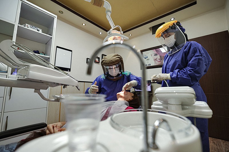 A dentist and assistant in full PPE treat a patient in a dental chair in their clinic