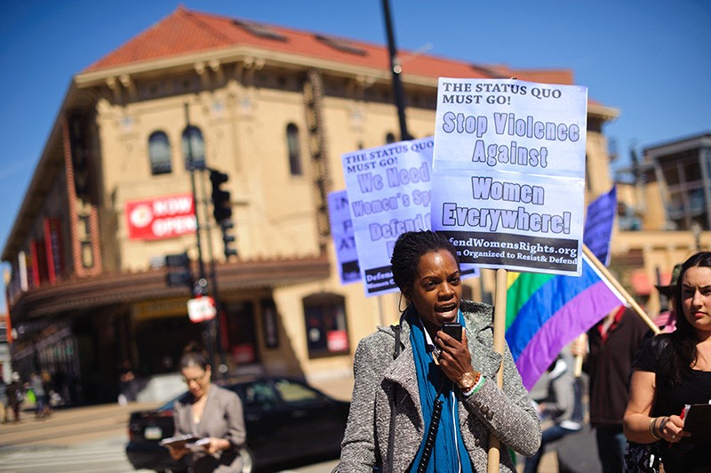 A woman speaks while others hold signs to protest against violence against women.