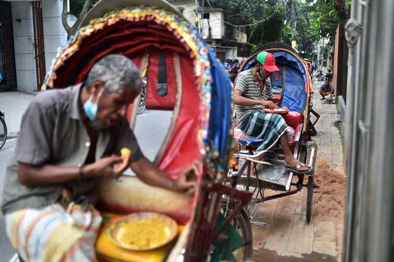 Men sit in their rickshaws eating from bowls in Dhaka