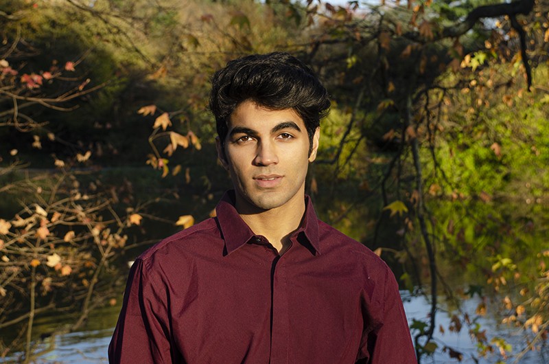 Saad Amer portrait taken in the woods with leaves on trees surrounding him.