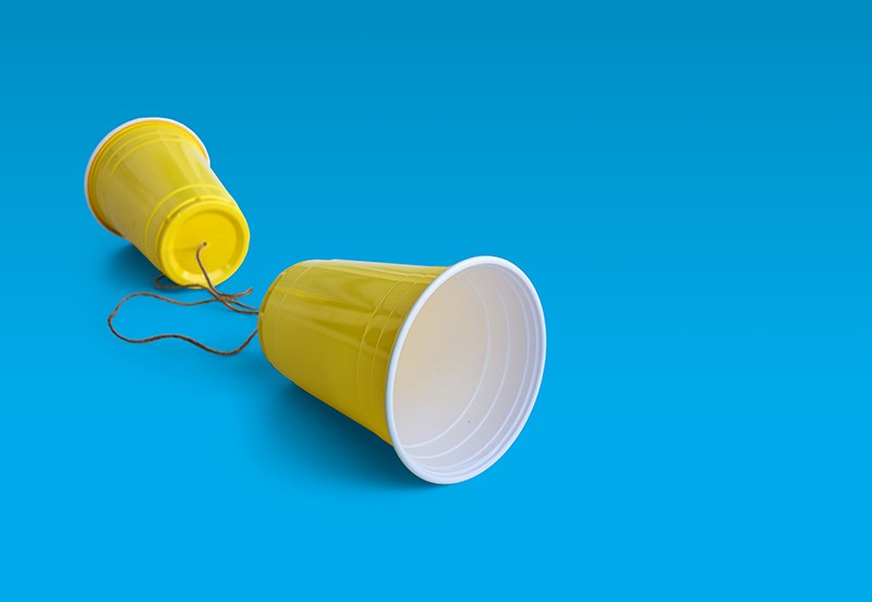 Two yellow plastic cups on a blue background attached by a string.