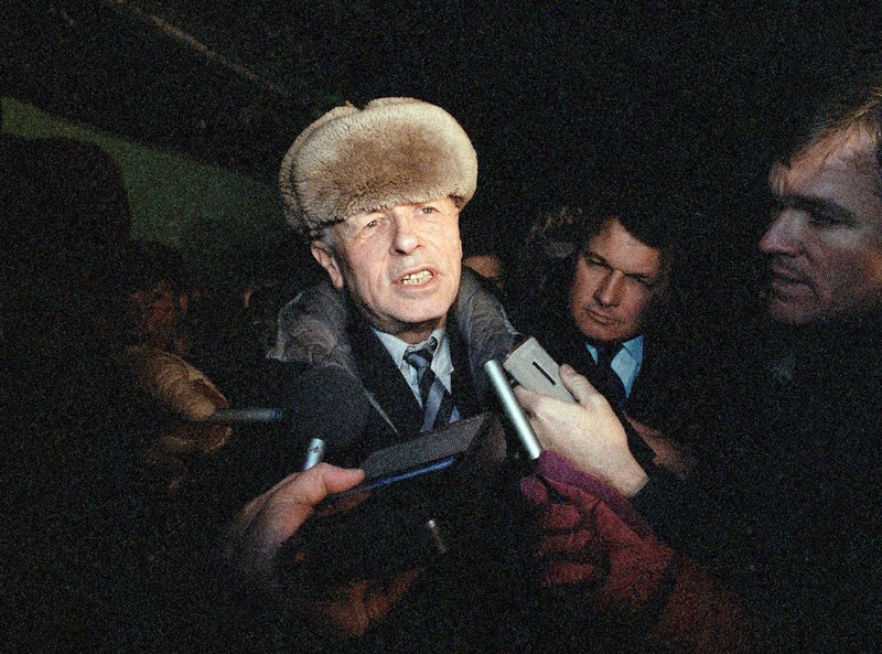 Andrei Sakharov wearing a hat is surrounded by press holding recording devices