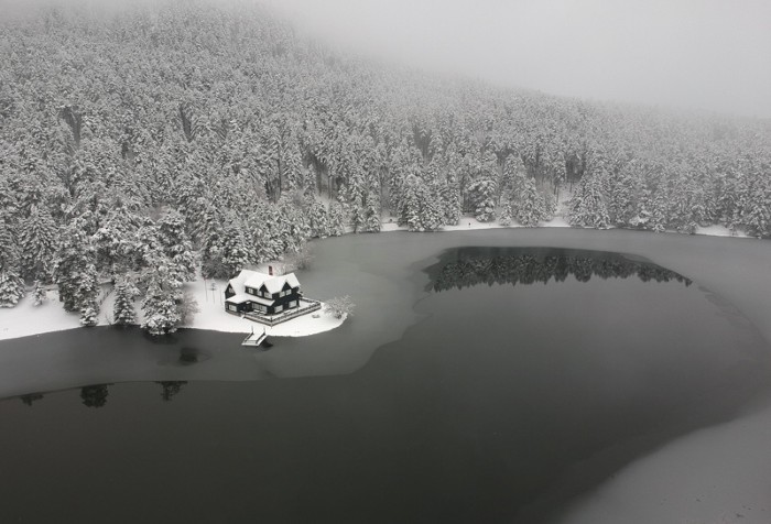 Aerial view of a partially frozen lake surrounded by snowy trees