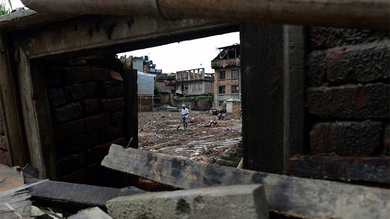 A nepalese man can be seen through a doorway of a collapsed house in Bhaktapur. Broken timber beams are in foreground