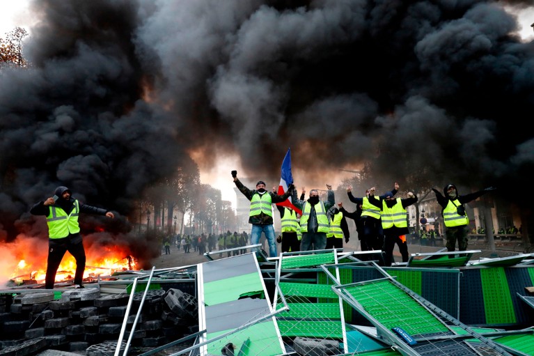 Yellow vests (Gilets jaunes) protestors shout slogans as material burns