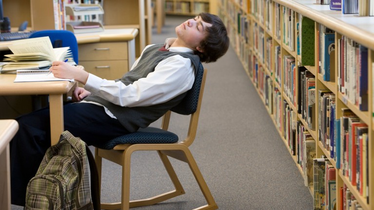 Teenager sleeping at desk in library.