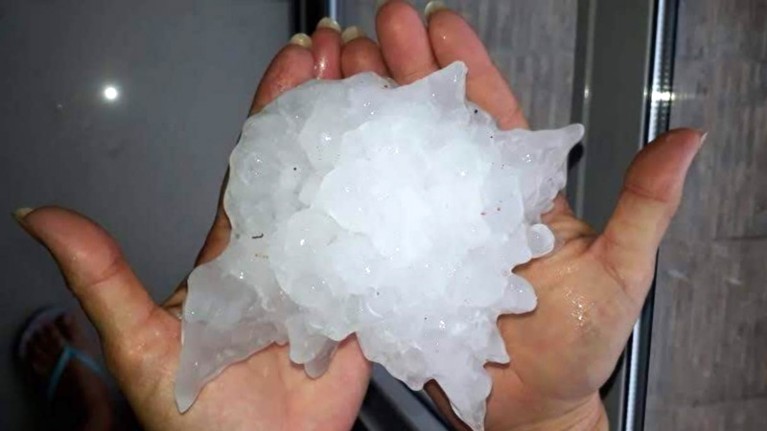 Two hands hold a giant hailstone.