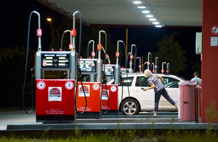 A woman checks her car between rows of red petrol pumps at a petrol station