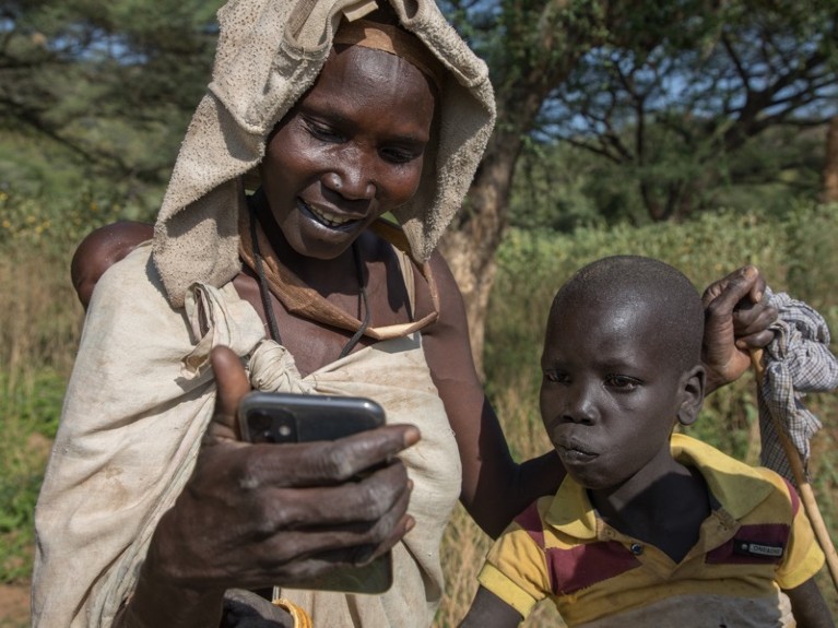 Mourning Larim tribe woman showing a mobile phone to her son.
