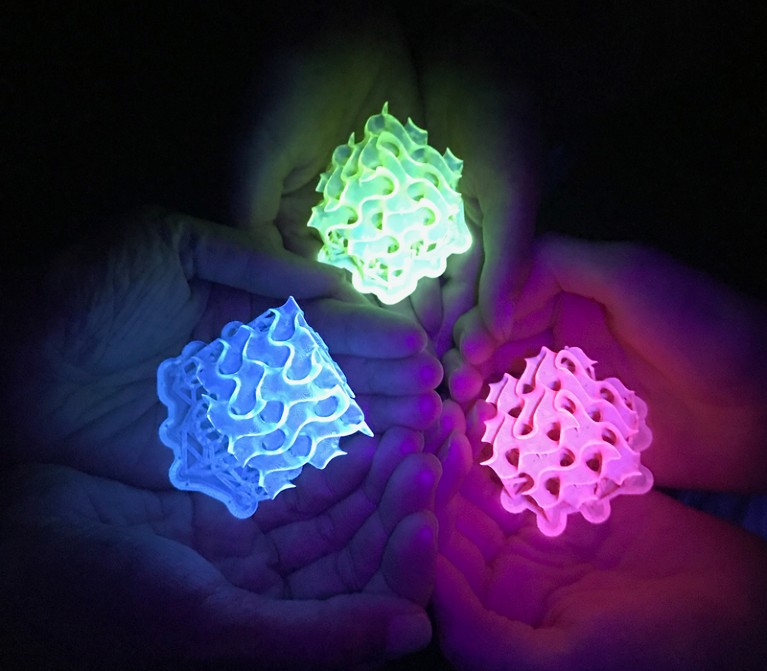 Hands holding glowing 3D-printed objects.
