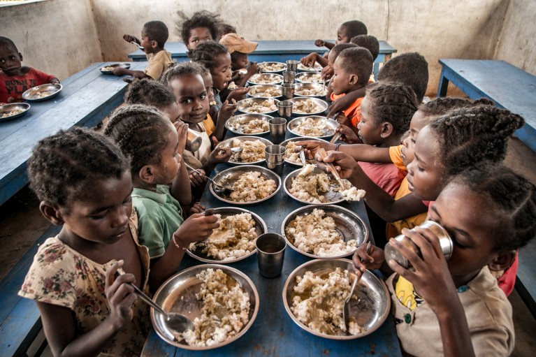 Primary school children sit at a long table eating their lunch in Madagascar