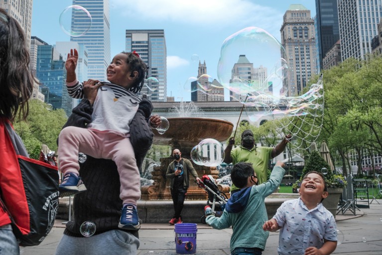 Children and adults play with bubbles in a park in a built up area of New York