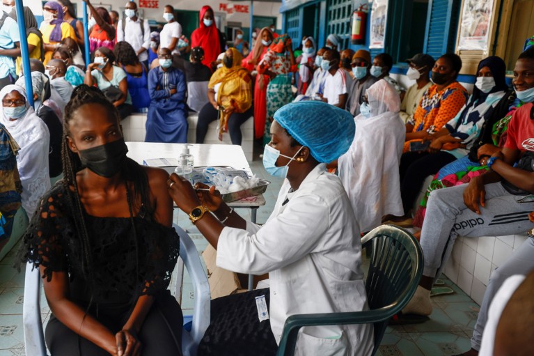 A nurse inoculates a woman surrounded by people wearing face masks at a hospital