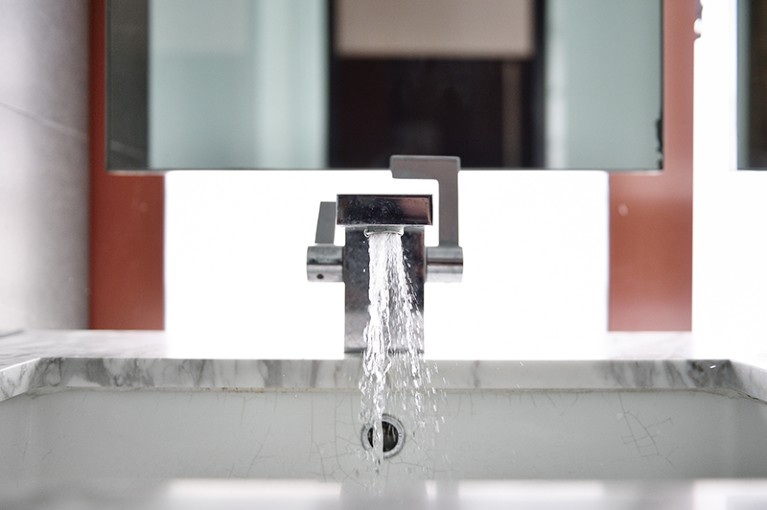 A luxury bathroom sink faucet with running water in a residence in Singapore.