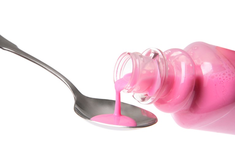 Pouring pink stomach medicine into a metal tablespoon.