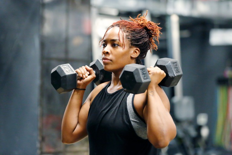 A young African American woman working out with dumbbells in the gym