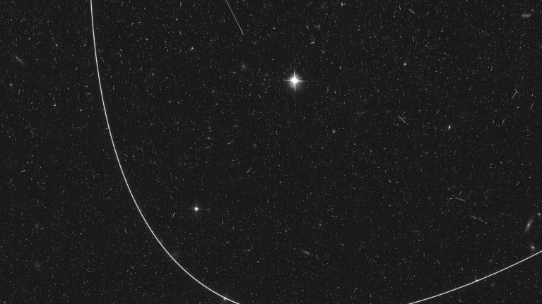 A black and white image of a curved satellite trail captured by the Hubble Space Telescope