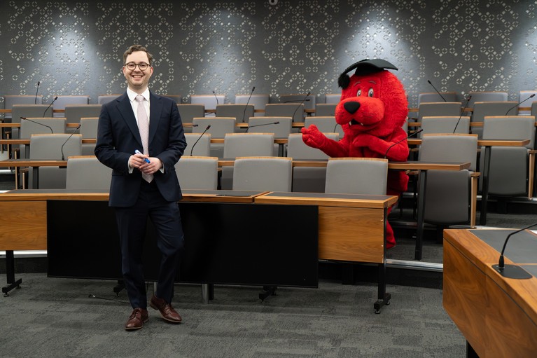 Andrés Gvirtz stands and Reggie the Lion mascot sits in an otherwise empty college lecture hall at King's College London.