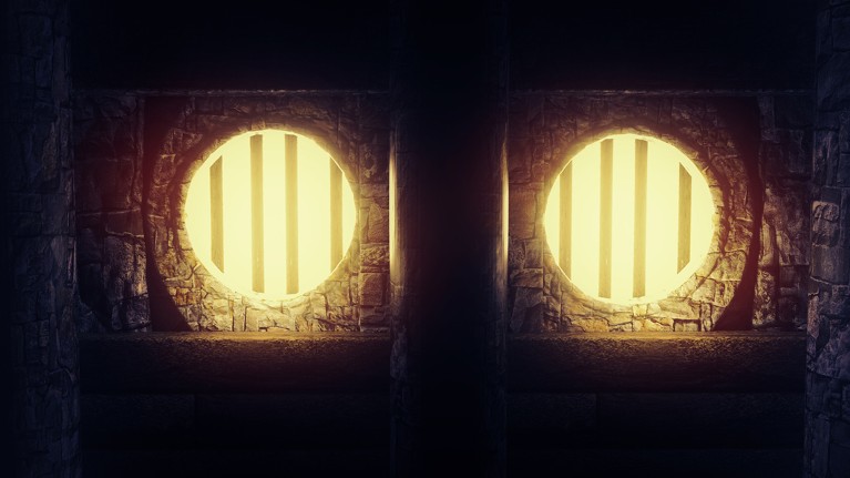 Light blazes from behind the bars that cross two round openings set in a rock wall, making them look like eyes
