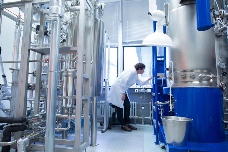 Technician in a white lab coat bends down to inspect a fermentation reactor