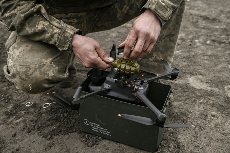 A Ukranian solder attaching a hand grenade to a shoebox-sized drone with four propellers