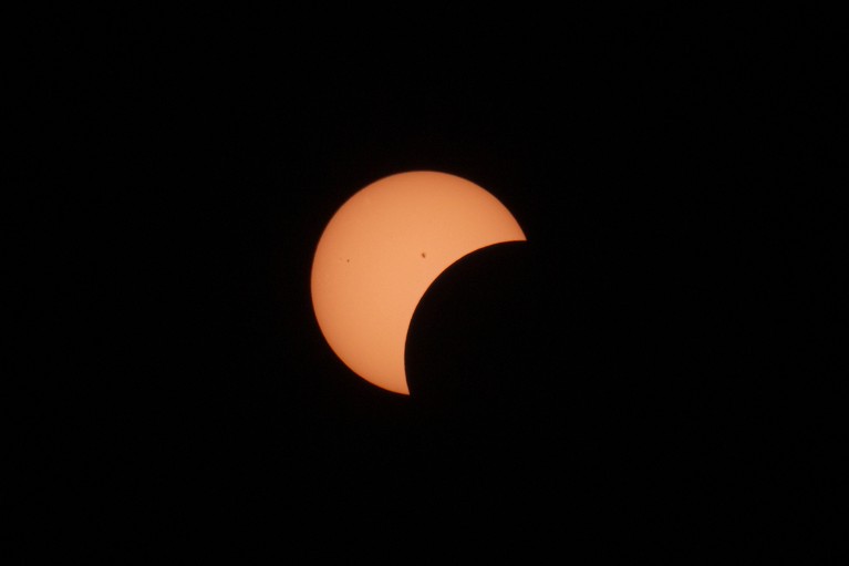 The Sun, orange and crescent-shaped, partially blocked in an eclipse.