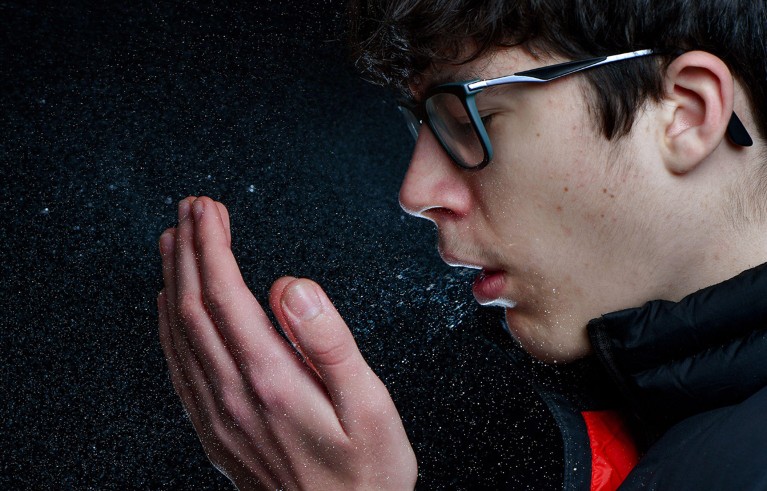 A high speed photograph illustrates the many droplets expelled into the air by a sneezing teenage boy.