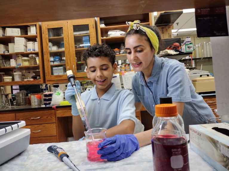 Taghreed Al-Turki and her son work together at a lab bench pipetting pink liquid from a beaker