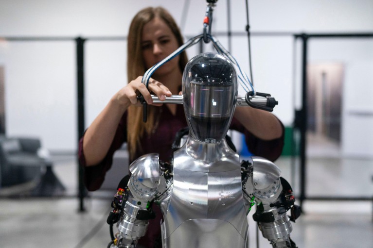 An engineer works on Figure AI's humanoid robot Figure 01 which has a metallic armour-like body and featureless head