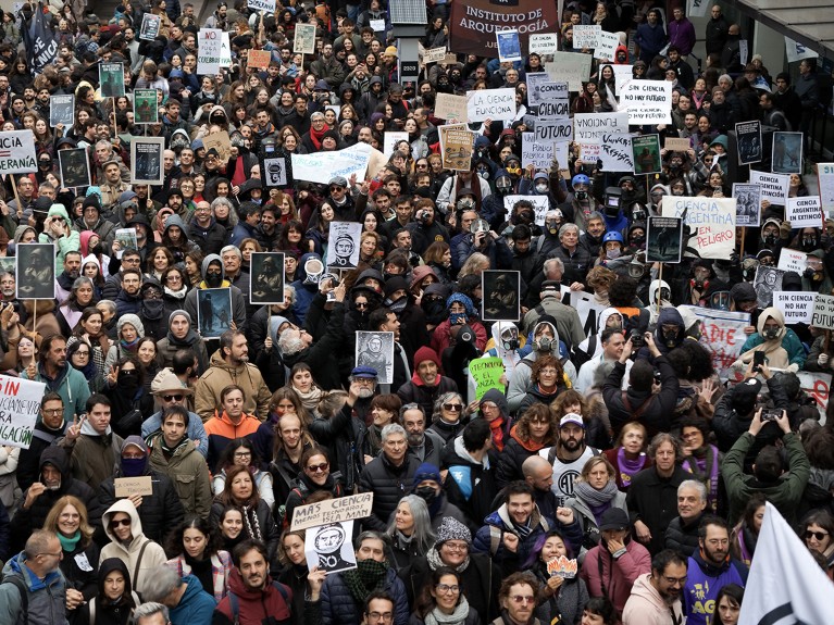 Crowds of people gather, march, and hold signs to protest the Argentinian government's dismantling of science.