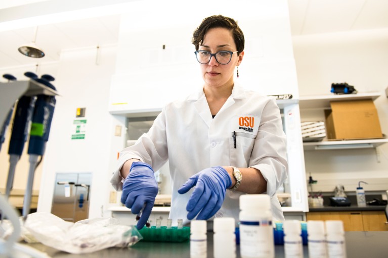 Tala Navab-Daneshmand wearing an OSU-branded lab coat and blue gloves handing wastewater samples in a laboratory