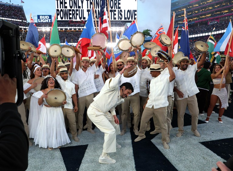Singer Bad Bunny performs onstage with a group of international musicians holding various countries' flags during the US Super Bowl LX in 2026.