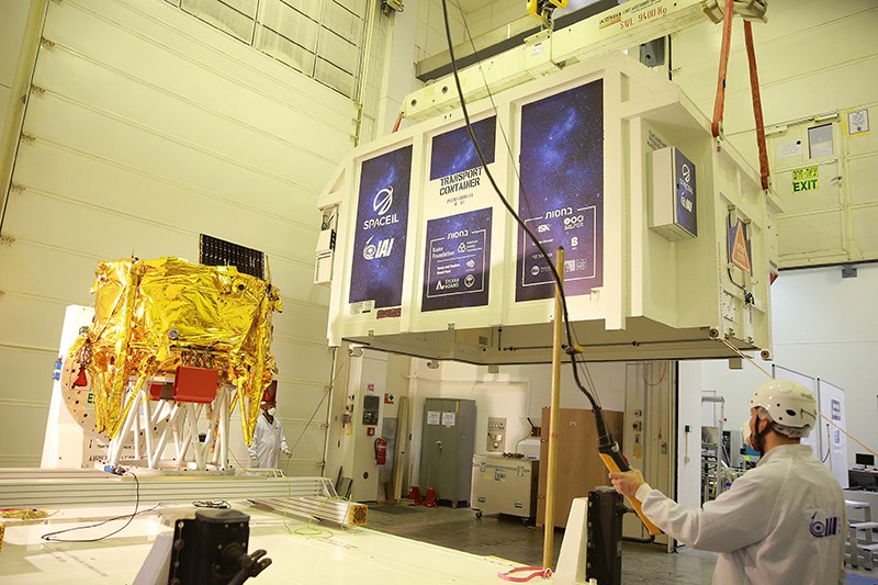 A man wearing safety gear uses an automated system to hoist a golden paper landing gear into a container.