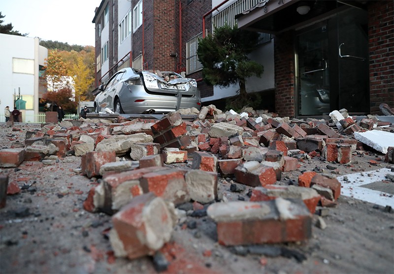 Bricks and debris from damaged buildings are lying on the ground in front of a damaged car in Pohang, South Korea.
