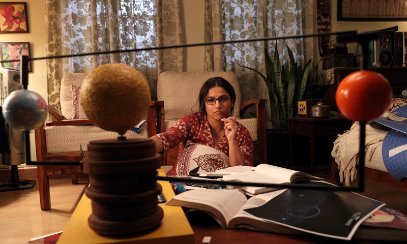 The actress Vidya Balan as project director Tara Shinde - sitting at a cluttered office in front of a solar system model.