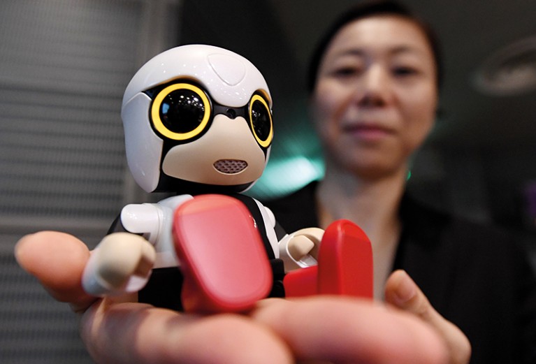 A woman holds a small robot in the palm of her hand