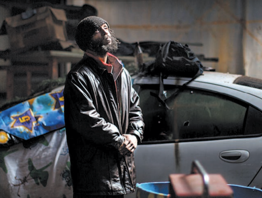 Charles Edward, who lives in a factory in Michigan, in an oversized coat staring upwards